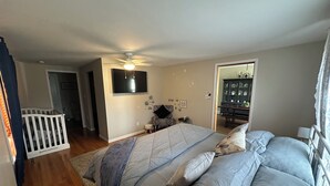 A bedroom with a bed, a ceiling fan, a television, a small table, and a cabinet with dishes.