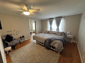 Une chambre à coucher avec un lit, des tables de chevet, un ventilateur de plafond, un tapis et une chaise.