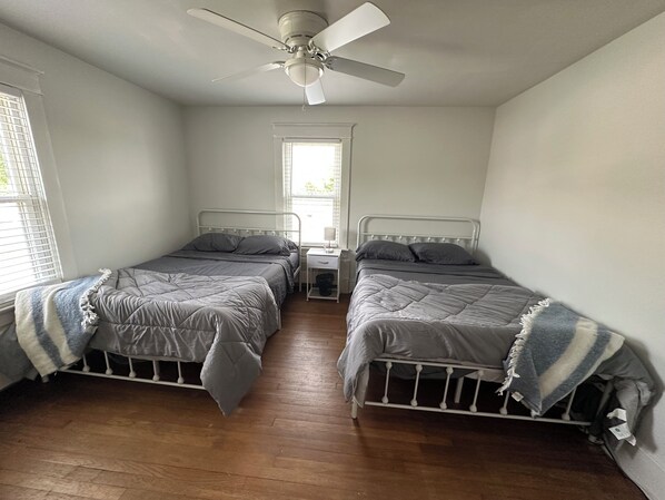 Une chambre avec deux lits, un ventilateur de plafond, une fenêtre et une table de chevet.
