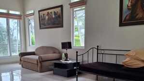 A spacious room with a large window, a bed, a sofa, and a painting on the wall. - Dagope Homestay (Lembang)