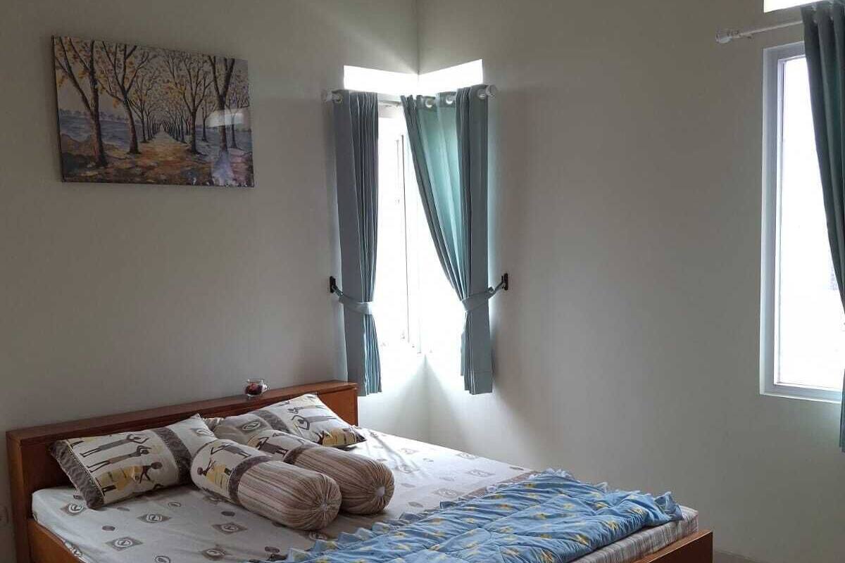 A bedroom with a wooden bed, a painting on the wall, and two windows with curtains.