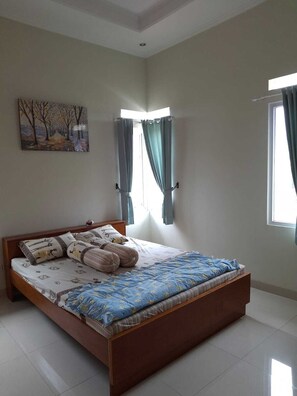 A bedroom with a wooden bed, a painting on the wall, and two windows with curtains. - Dagope Homestay (Lembang)
