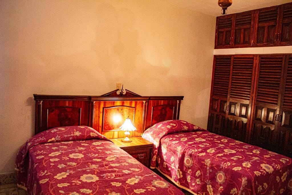 Una habitación con dos camas, una mesita de noche con lámpara y muebles de madera.