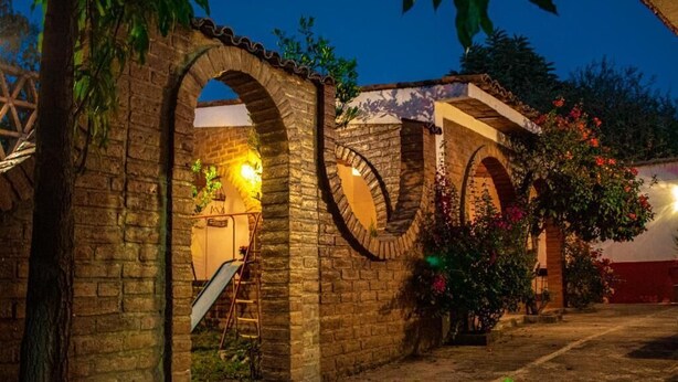 A courtyard with stone arches, a staircase, and a garden with flowering plants. - Villa Flores (Mascota)