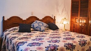 A bed with a floral bedspread, a wooden headboard, and a bedside lamp. - Villa Flores (Mascota)