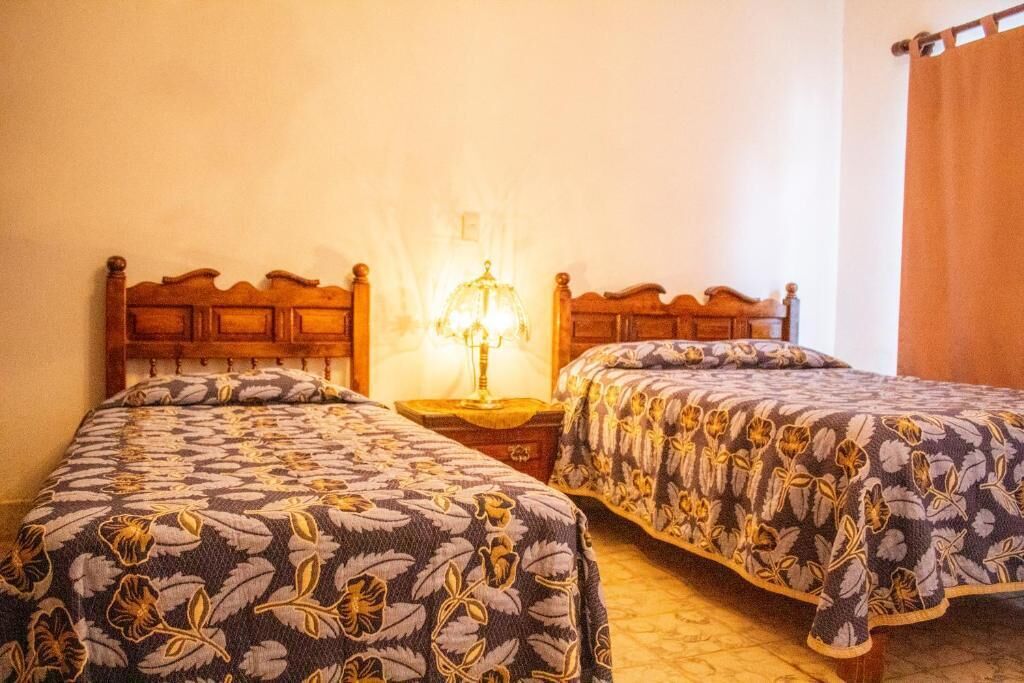 A room with two wooden beds, a nightstand with a lamp, and a window with curtains.