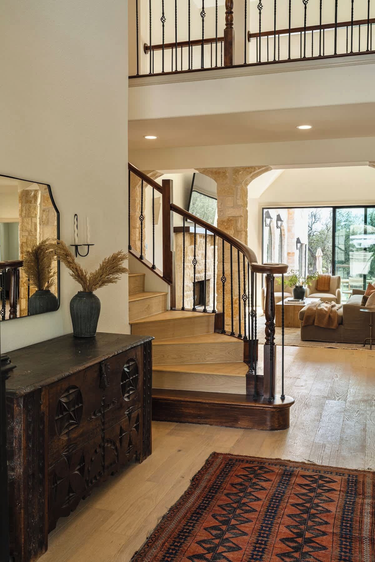 A spacious living area with a wooden staircase, a large mirror, and a view of the outdoors.