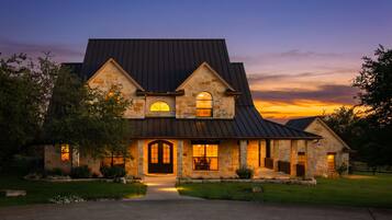 A large stone house with a dark roof, a front entrance, and a well-lit interior.
