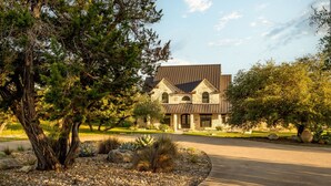A modern house with a stone facade, a sloped roof, and a driveway leading to the entrance. - Deep Eddy Ranch: 10 Acres, Pool, Pickleball, Sauna (Dripping Springs)
