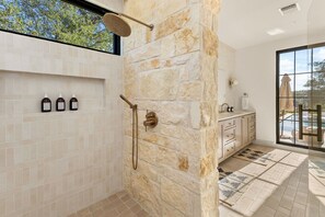 A bathroom with a stone shower wall, a window, and a view of the outdoors. - Deep Eddy Ranch: 10 Acres, Pool, Pickleball, Sauna (Dripping Springs)