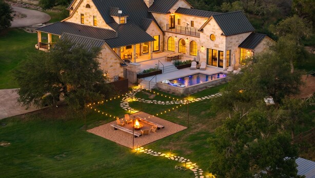 A large stone house with a swimming pool, outdoor seating, and a fire pit.