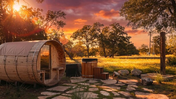 A wooden barrel-shaped structure with a door, a barrel, and a stone pathway. - Deep Eddy Ranch: 10 Acres, Pool, Pickleball, Sauna (Dripping Springs)
