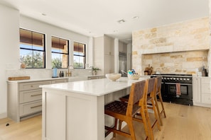 A modern kitchen with a large island, white cabinetry, and a stone fireplace.