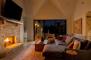 A modern living room with a stone fireplace, leather sofas, a flat-screen TV, and a large window.