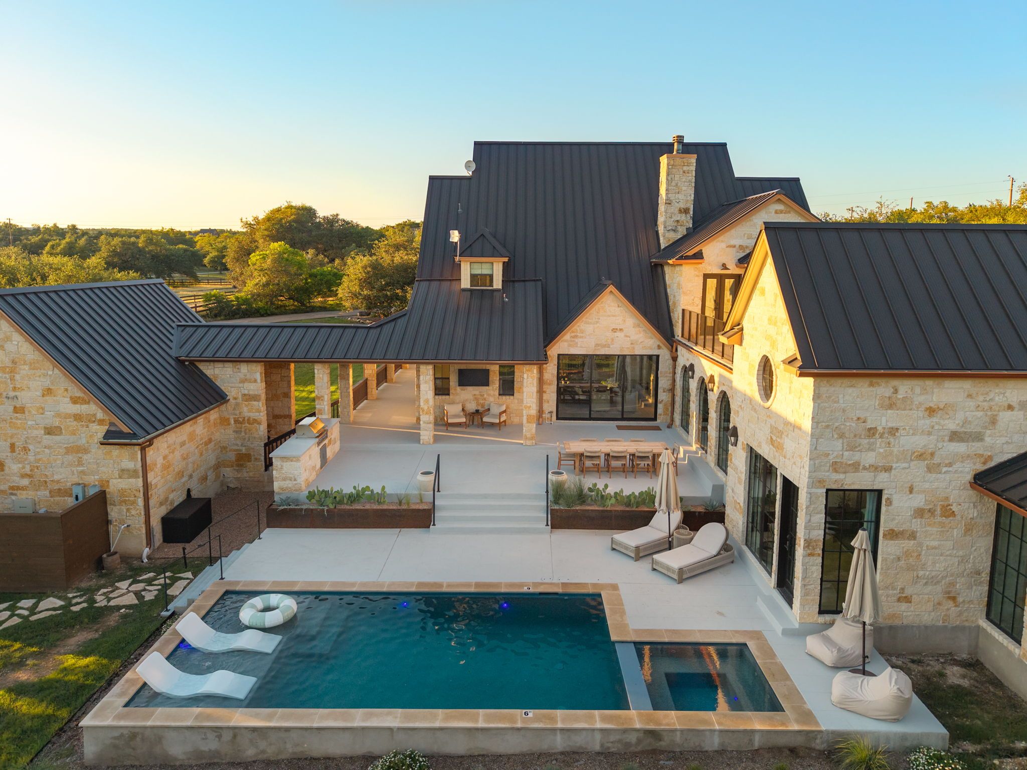 Una casa grande con piscina, mobiliario exterior y fachada de piedra.