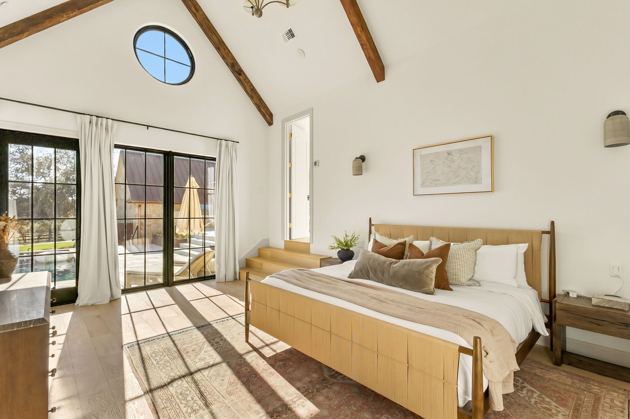 A bedroom with a large bed, a window with curtains, a view of a pool, and a wooden ceiling.
