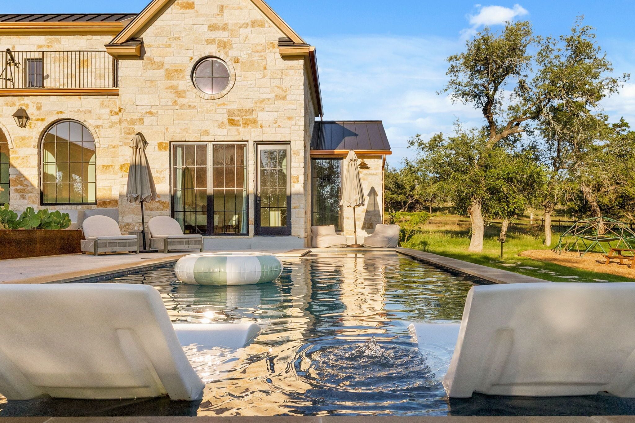 Una casa de piedra con piscina, mobiliario de exterior y una pérgola.