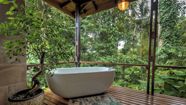 Eine freistehende Badewanne auf einer Holzterrasse mit Blick auf üppiges Grün.