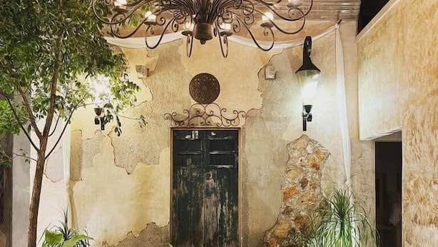 An outdoor patio with a wrought iron chandelier, a stone wall, and a door. - Casa Ek: House•Safe•Fast WiFi•Pool•Walkable  area (Mérida)
