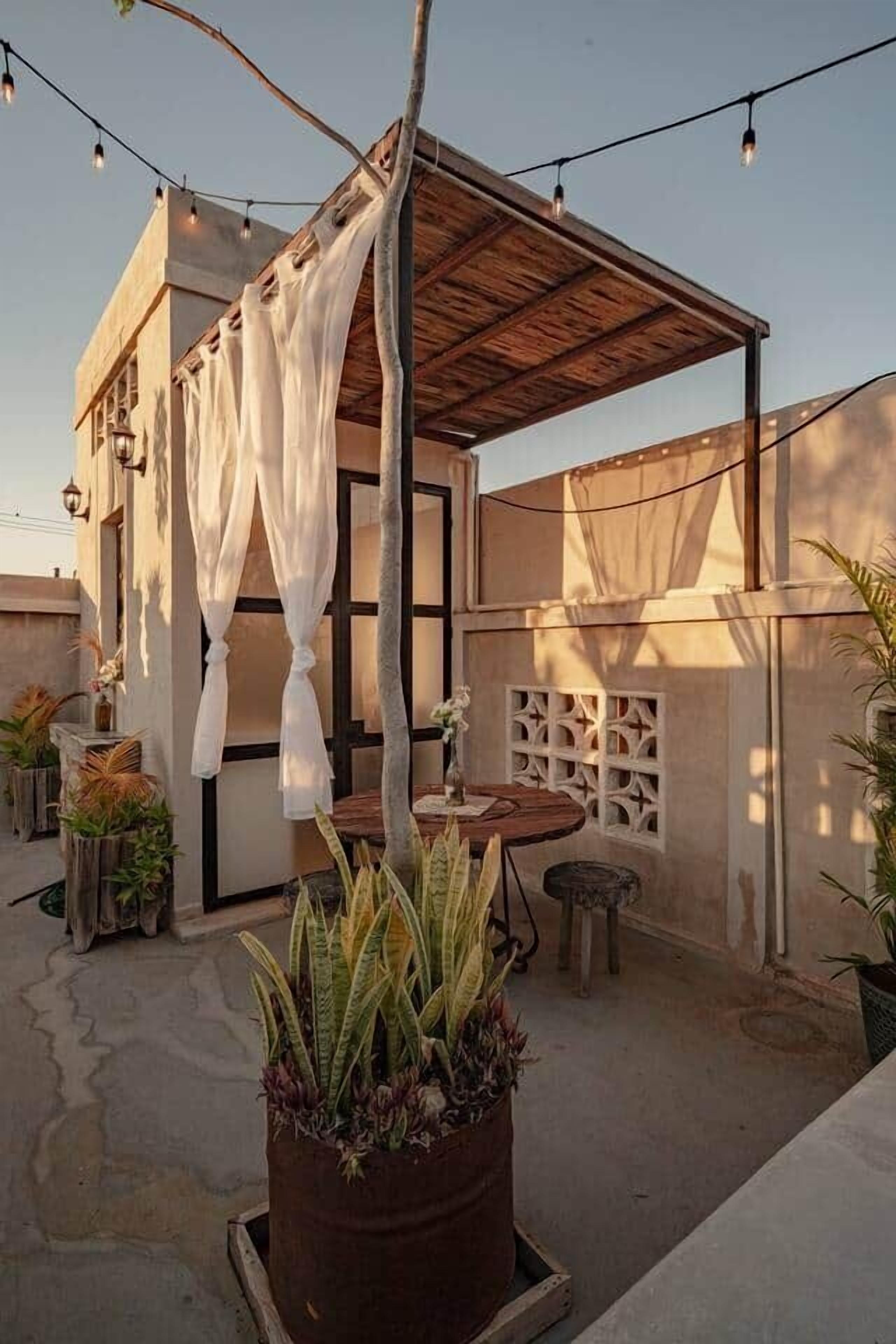 An outdoor patio area with a wooden pergola, string lights, a table, and potted plants.
