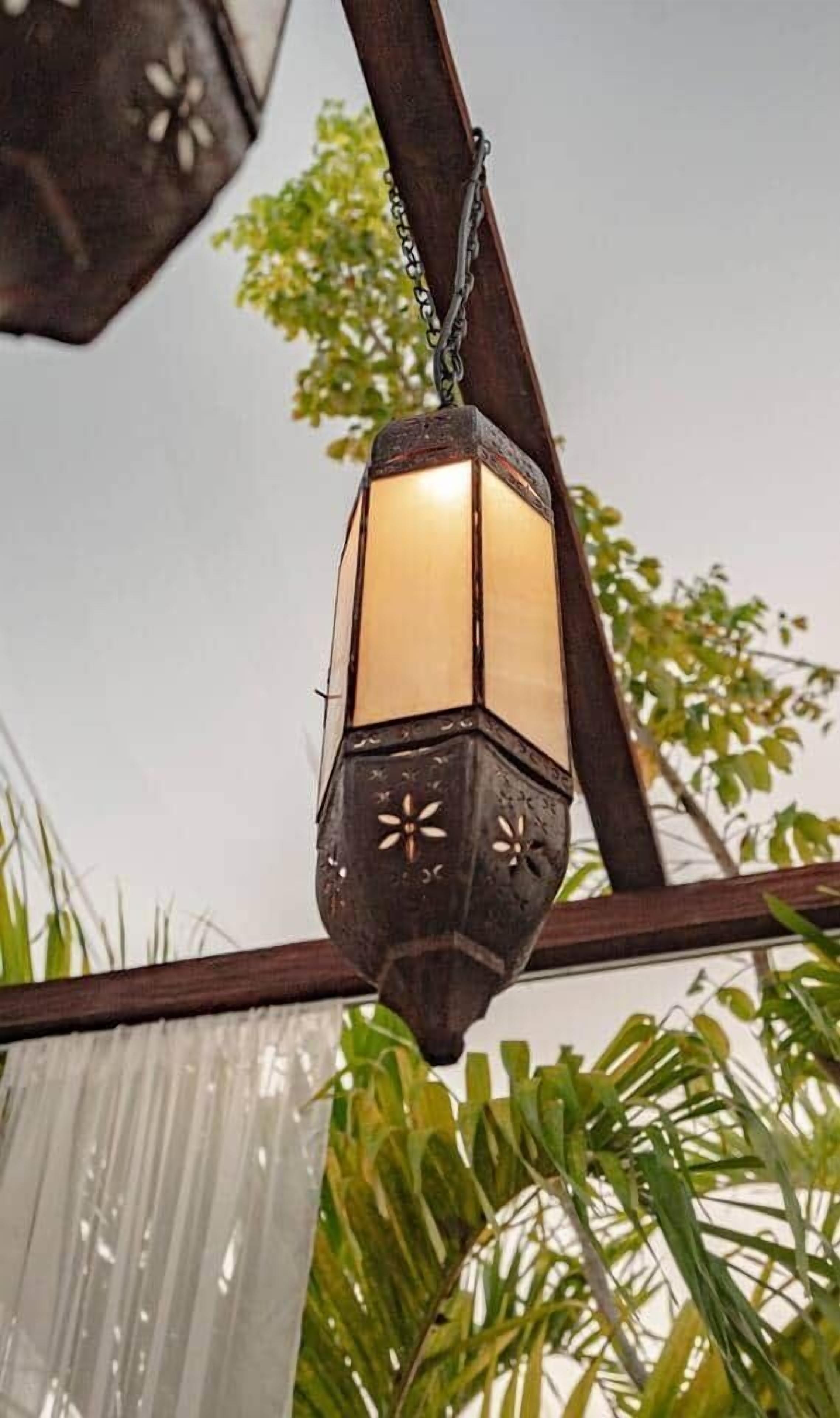 A hanging lantern with a chain, a wooden structure, and green foliage in the background.