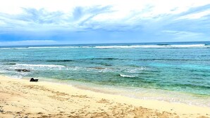 A beach with clear water, a sandy shore, and a boat on the sand.