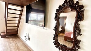 A room with a wooden staircase, a large mirror, and a bed with a pink bedspread.
