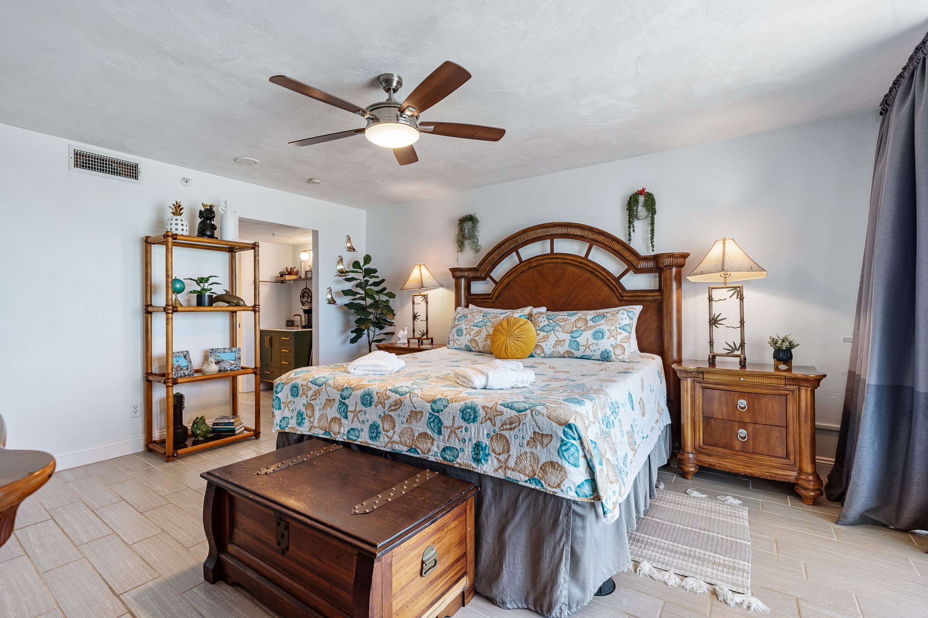 Une chambre à coucher comprenant un lit, une table de chevet en bois, une commode, un ventilateur de plafond et une bibliothèque.