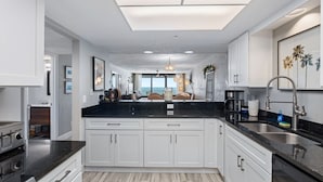 Una cocina moderna con armarios blancos, encimera negra y vistas al área de estar.