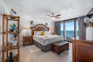 Ein Schlafzimmer mit Bett, Nachttischen, einem Schrank, einem Holzkleiderschrank, einem Deckenventilator und Blick auf den Ozean.