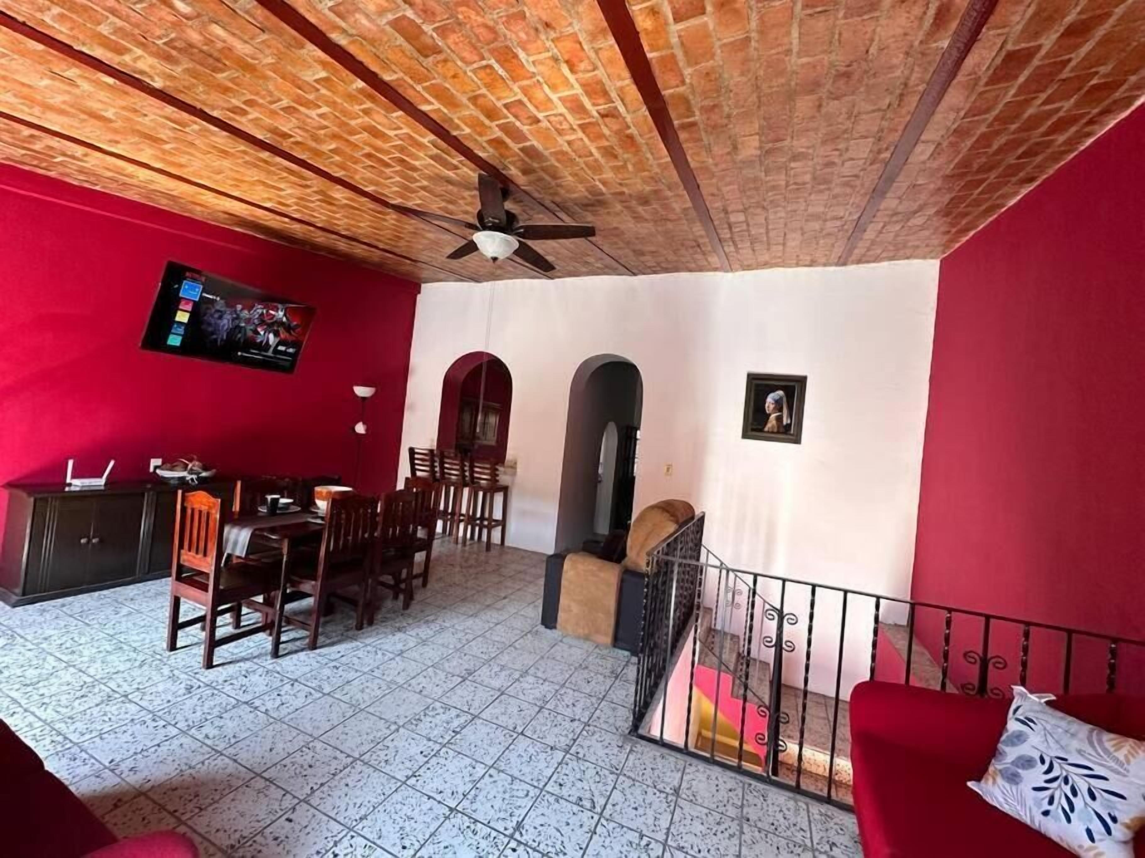 Comedor con televisor, sillas de madera y sofá rojo.