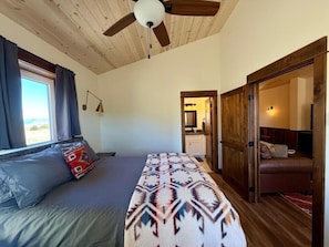 Un dormitorio con cama, ventilador de techo, ventana con cortinas y vistas al exterior.