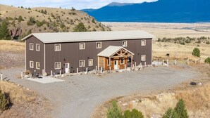 A two-story building with a central wooden structure, a gravel driveway, and a mountainous backdrop. - Elk Suite: Epic Paradise Valley Views will amaze. (Emigrant)