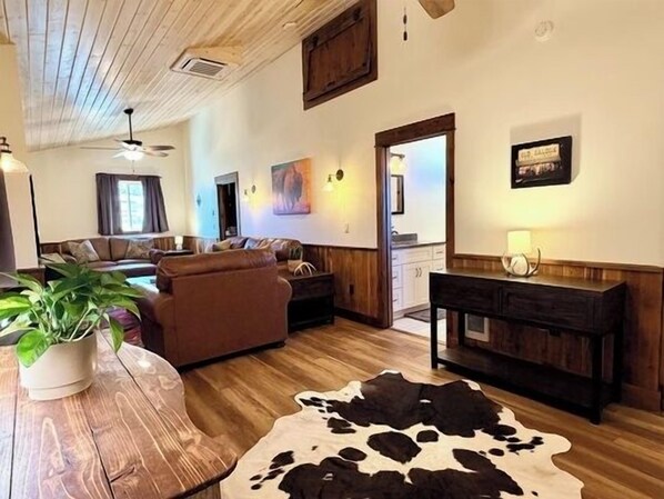 Una sala de estar con techo de madera, un sofá, una mesa de centro y un tapiz de cuero de vaca.