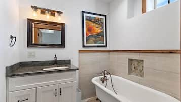 Een badkamer met een vrijstaand bad, een wastafelmeubel met een wastafel en een lijstwerkkunstwerk aan de muur.