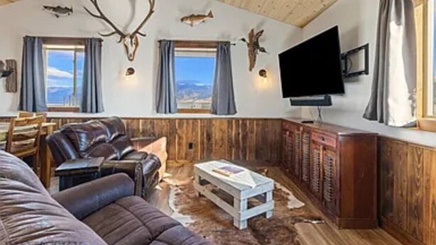 En rustik inredning med en soffa i läder, ett vitt soffbord, träskåp och uppstoppade djurhuvuden som hänger på väggen.