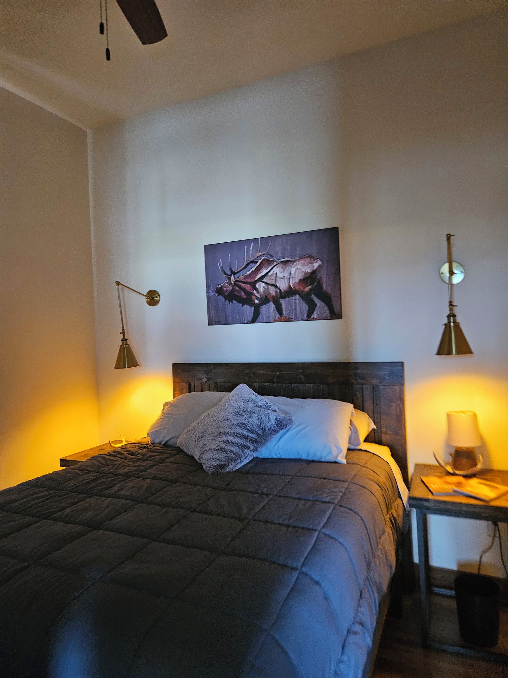 A bedroom with a bed, a painting, two bedside lamps, and a nightstand with a lamp.