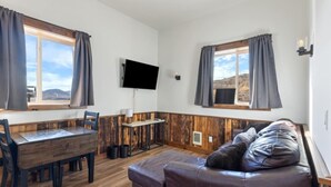 Ett rum med ett matbord i trä, en soffa, en platt-TV och ett fönster med gardiner.