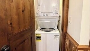 Ett tvättrum med tvättmaskin och torktumlare, en trädörr och ett litet fönster.