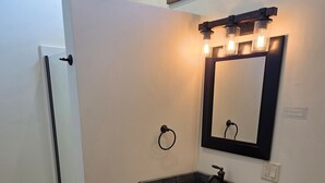 A bathroom with a white toilet, a sink with a marble countertop, a mirror with lights, and a towel ring. - Rainbow Trout Suite in Emigrant (Emigrant)