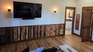 A room with a flat-screen TV mounted on the wall, wooden paneling along the lower half of the wall, a ceiling fan, and a wooden door. - Rainbow Trout Suite in Emigrant (Emigrant)