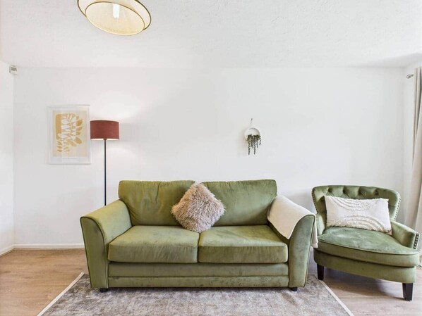 Ein grünes Sofa und ein Sessel in einem Raum mit weißer Wand, einer Stehlampe und einem gerahmten Bild.