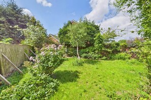 Ein gepflegter Garten mit verschiedenen Pflanzen und Bäumen, einem Holzzaun und blauem Himmel.