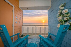 A balcony with two turquoise chairs, a view of the sunset over the ocean, and a decorative wall with flowers. - New! Oceanfront / Pool / Boat / Surf / Kayak, Swim (Virginia Beach)