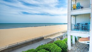 A beach view from a building with a balcony, a concrete walkway, and a small garden area. - New! Oceanfront / Pool / Boat / Surf / Kayak, Swim (Virginia Beach)