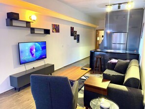 A modern living room with a flat-screen TV, a sofa, a coffee table, and a kitchen area with a countertop and stools. - Cosy Flat Neartaksim and Nişantaşi (Istanbul)