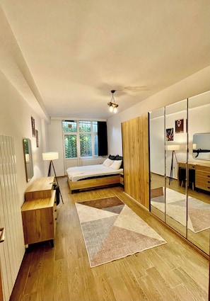 Quarto com cama de madeira, escrivaninha, espelho e janela com vista para o verde.