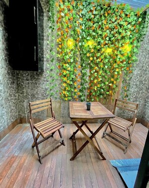 Um canto com uma mesa de madeira e duas cadeiras, parede com folhagem verde e luzes amarelas, e piso de azulejos.