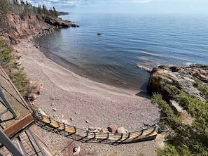 Ein Strand mit einer Holzpromenade, die zum Ufer führt, umgeben von felsigem Gelände und Bäumen.