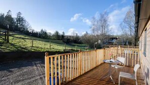 A wooden deck with a railing, outdoor seating, and a view of a green landscape.